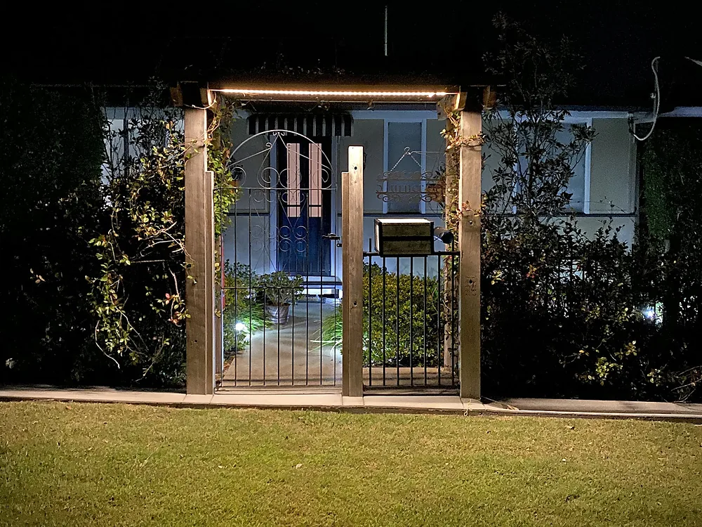 A front gate arch lit at night with warm LED strip lighting and garden lights