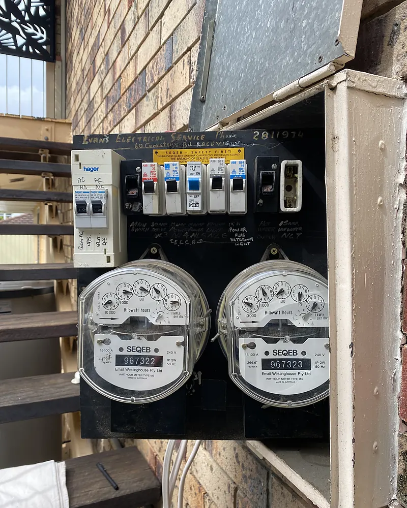 An older meter board with two analogue meters and circuit breakers on a brick house