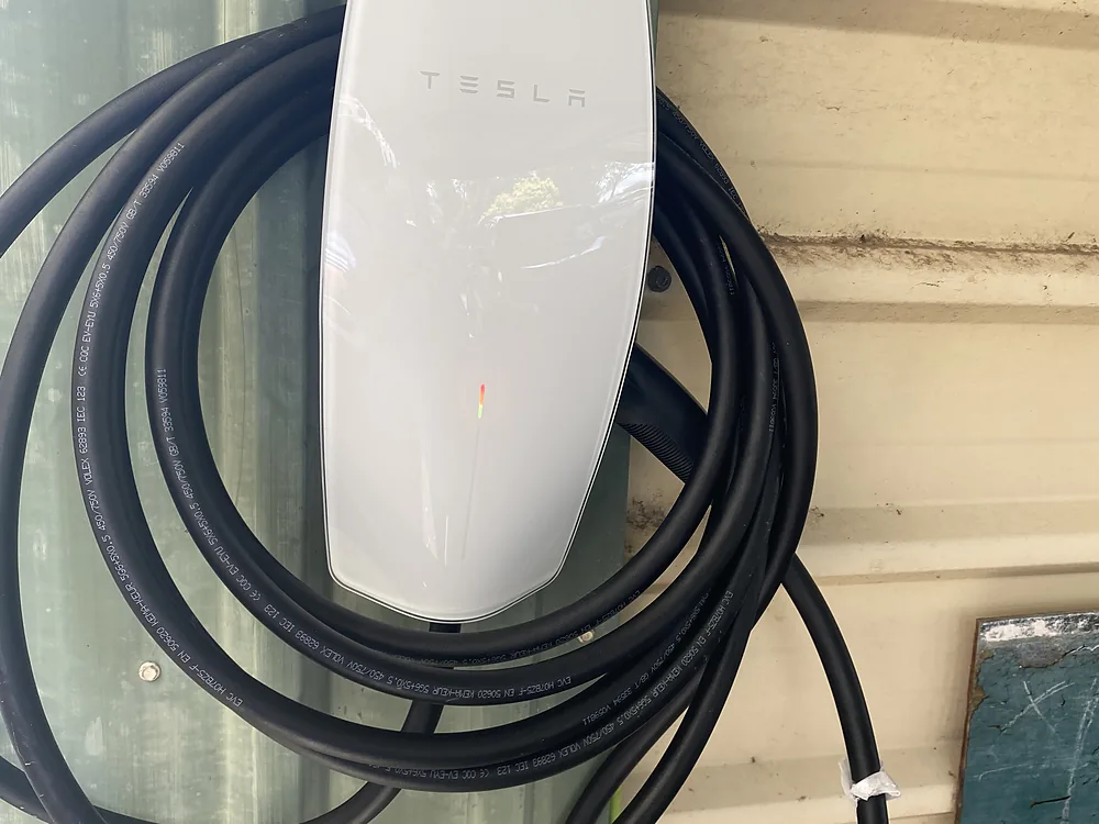 A white Tesla Wall Connector EV charger mounted on a wall with its cable coiled
